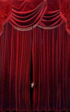 a person peeking out from behind a red curtain with their hand in the hole between them