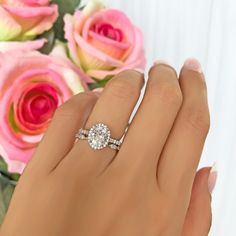 a woman's hand with a diamond ring on it and pink roses in the background