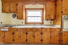 an empty kitchen with wooden cabinets and white stove top oven in the center, next to a window