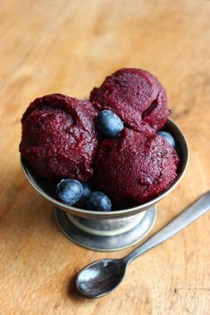 three blueberry muffins in a metal bowl with spoon on the wooden table