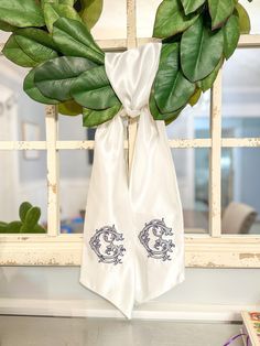 a pair of white cloths tied to a window sill with green leaves on it