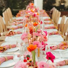 a long table is set with pink and orange flowers, candles and napkins on it