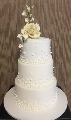 a three tiered wedding cake with white flowers on top and pearls around the edges