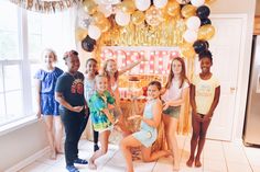 a group of children standing in front of a birthday cake and balloons on the wall