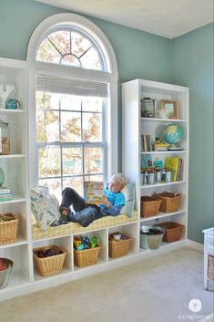 a child sitting on a window seat in front of a book shelf filled with books