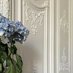 a vase filled with blue flowers sitting on top of a table next to a wall