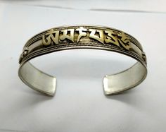 "Here's a beautiful vintage cuff bracelet with bronze overlay lettering spelling out the beautiful Buddhist Chant \"Nam Myoho Renge Kyo\" in Sanskrit. This bracelet was hand-crafted by an unidentified Native silversmith, and decorated with traditional Tibetan motifs, delicately twisted wire, and the applied Bronze letters. It's 13.5 mm wide, and measuring on the inside, this bracelet is 2 & 5/8ths inches across, about 1 & 7/8ths inches front to back, with a 1 & 1/4 inch gap between t Antique Etched Bangle Cuff Bracelet, Traditional Sterling Silver Etched Cuff Bracelet, Symbolic Stamped Cuff Bangle Bracelet, Silver Spiritual Brass Bangle, Bohemian Engraved Antique Silver Cuff Bracelet, Nam Myoho Renge Kyo, Symbolic Stamped Cuff Bracelet, Spiritual Silver-colored Brass Bangle, Vintage Hand-tooled Brown Cuff Bracelet