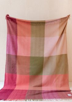 a pink and green checkered blanket sitting on top of a white table next to a wall