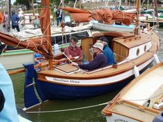 two people sitting in a small sailboat on the water with other boats behind them