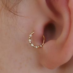 a close up of a person's ear wearing a gold nose ring with white stones