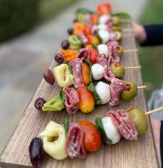 several skewers of meat and vegetables are lined up on a long wooden board