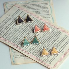 three small triangle shaped pins sitting on top of an open book with writing underneath them