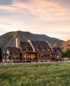 a large house sitting in the middle of a lush green field next to a mountain