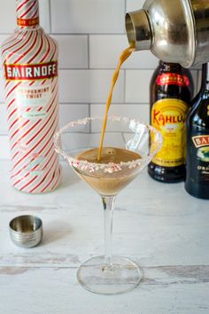 a martini being poured into a glass with candy canes and bottles in the background