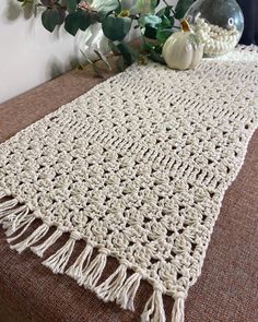 a white crocheted table runner with tassels and flowers in the background