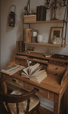 an open book is sitting on top of a wooden desk next to a chair and lamp