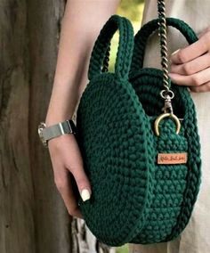 a woman holding a green crocheted purse with a chain around the strap and clasp