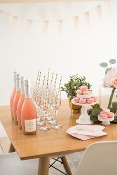 a table topped with pink cupcakes and wine glasses next to bottles of champagne