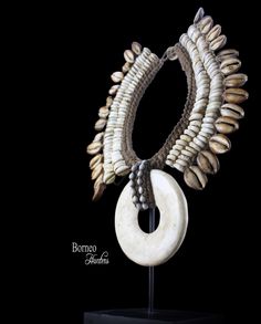 Vintage Papua New Guinea brown rope necklace, composed of a circular White Currency Coral Shell drop pendant. The collar is decorated with two rows of white Cowrie Shells and a row of large Brown patterned Cowries. The Coral Pendant is, approximately 4.75 inches in diameter. The inner diameter of the band of the necklace is 4.4 inches, and the maximum outer diameter of the necklace is 11 inches. The necklace has a drop length of inches. The necklace is attached, at the top, by a beige braided Ro Bohemian Round Ceremonial Necklace, Bohemian Round Necklace For Ceremonial Use, Bohemian Round Necklace For Ceremonial Occasions, Unique Ceremonial Necklace, White Ceremonial Pendant Necklaces, White Pendant Necklace For Ceremonial Occasions, White Bohemian Ceremonial Necklace, Unique Round Necklaces For Ceremonial Use, Unique Round Necklaces For Ceremonial Occasions