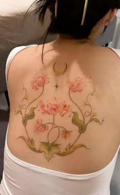 the back of a woman's shoulder with flowers and a crescent tattoo on it