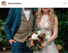 a man and woman standing next to each other in front of some bushes with flowers