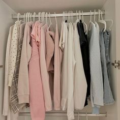 a closet filled with lots of clothes and sweaters hanging from hooks on the wall