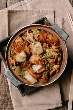 a bowl filled with meat and vegetables on top of a table next to chopsticks