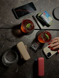 a woman's hand holding a cell phone next to some drinks and other items