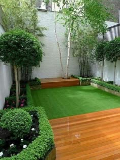 small garden with wooden decking and green grass in the center, surrounded by trees