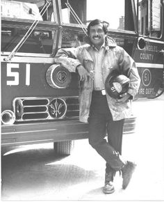 a black and white photo of a man standing in front of a firetruck