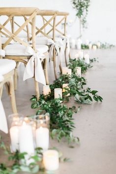 a row of chairs with candles and greenery on the floor next to each other