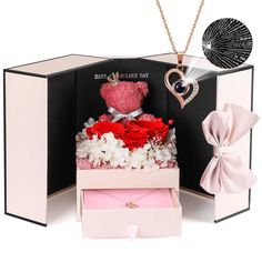 a pink box with flowers and a teddy bear in it is open to show its contents