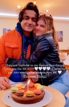 a man and woman sitting next to each other in front of a cake with candles on it