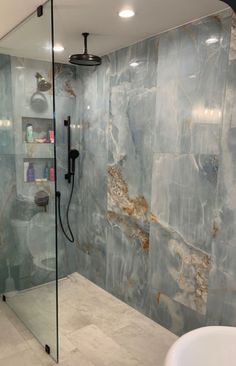 a bathroom with a glass shower door and marble tile on the walls, along with a white sink