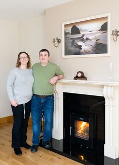 two people standing next to each other in front of a fireplace