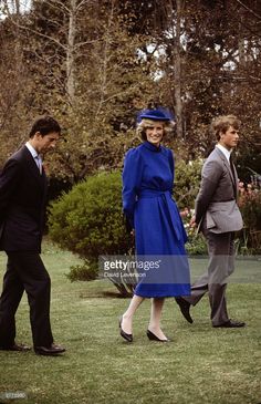 two men and a woman are walking in the grass with one man wearing a suit