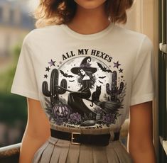 Embrace your witchy side with this "All My Hexes Live in Texas" t-shirt, combining a touch of Southwestern charm with spooky Halloween vibes! This unique design features a glamorous witch riding her broomstick, a black cat by her side, cacti, bats, and a glowing jack-o'-lantern, making it the perfect tee for Halloween enthusiasts and witchcraft lovers. Whether you're celebrating Halloween in style or just want to show off your witchy spirit year-round, this shirt is ideal for Halloween parties o Texas Halloween, Witch Lovers, Lantern Making, Witch Tshirt, Halloween Apparel, Halloween Vibes, Comfort Design, Halloween Parties, Halloween T Shirt