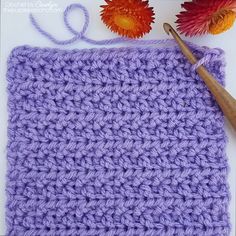 the crochet square is next to a flower and a pair of knitting needles