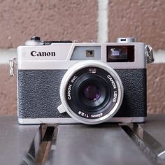 an old camera sitting on top of a wooden table next to a brick wall with the word canon printed on it