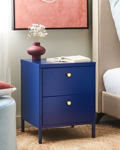 a blue nightstand next to a bed with a painting on the wall above it and a vase filled with flowers