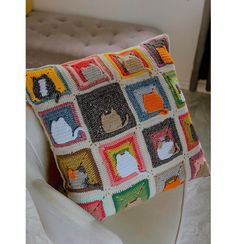 a crocheted pillow with cats and dogs on it sitting on a white chair