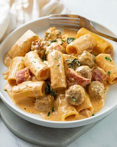 a white bowl filled with pasta and meat covered in sauce on top of a table