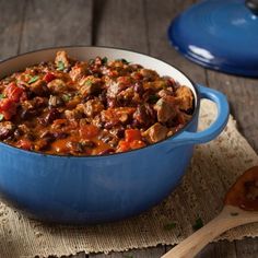 a blue pot filled with meat and vegetables on top of a table next to a wooden spoon