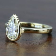 a yellow gold engagement ring with a pear shaped diamond on the top and bottom, sitting on a wooden surface