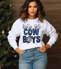 a woman standing in front of a christmas tree wearing a white sweatshirt with the words, let's go cow boys on it