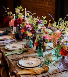 a wooden table topped with lots of plates and vases filled with different colored flowers