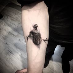 a person with a tattoo on their arm holding onto a small bear that is sitting on a branch