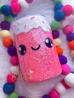 a pink cup with sprinkles on it sitting next to pom - poms