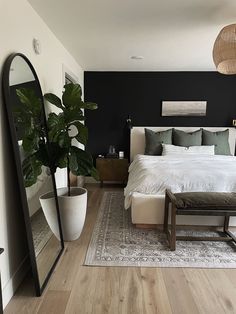 a bedroom with a bed, mirror and plant on the floor in front of it