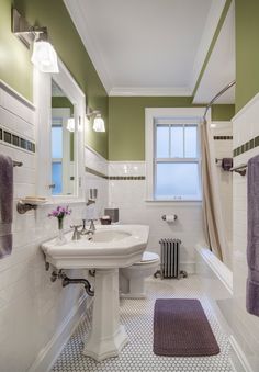 a bathroom with green walls and white tile on the floor, along with purple rugs